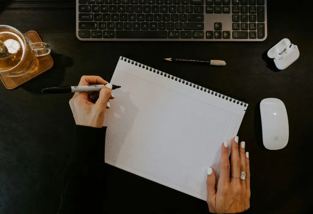una mujer organizando sus finanzas. Aparece con un cuaderno para apuntar cosas. Una taza de té. Sus auriculares y boligráfos.
